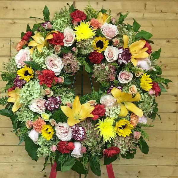 Large circular floral wreath with mixed roses, lilies, and sunflowers