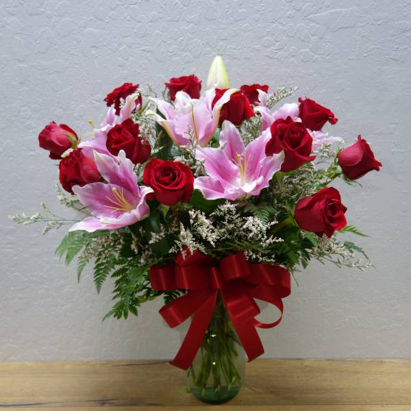 Bouquet of red roses and pink lilies in a glass vase with a red ribbon