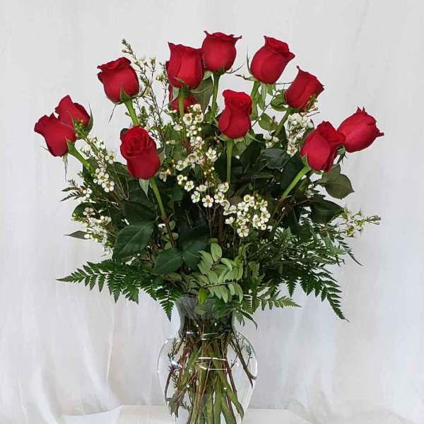Red roses arranged in a clear glass vase with small white filler flowers.