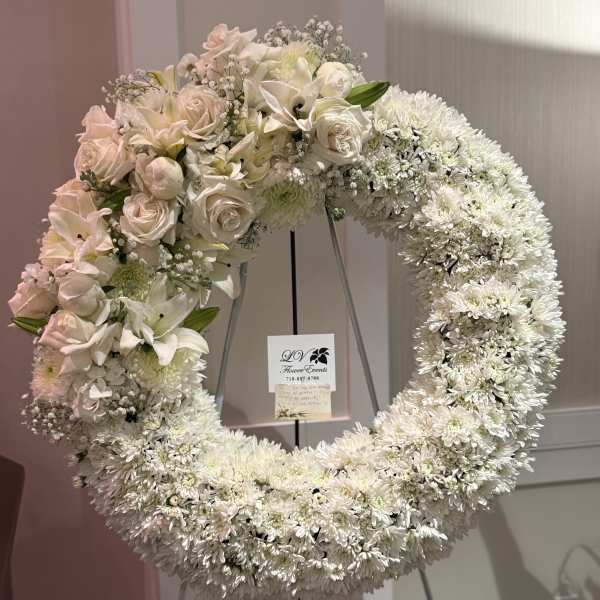 Large white floral wreath on a stand with pale pink roses and lilies