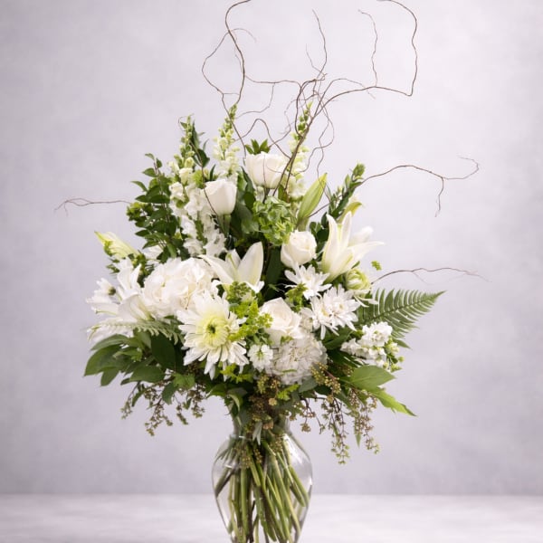 White floral arrangement in a clear glass vase with curly branches