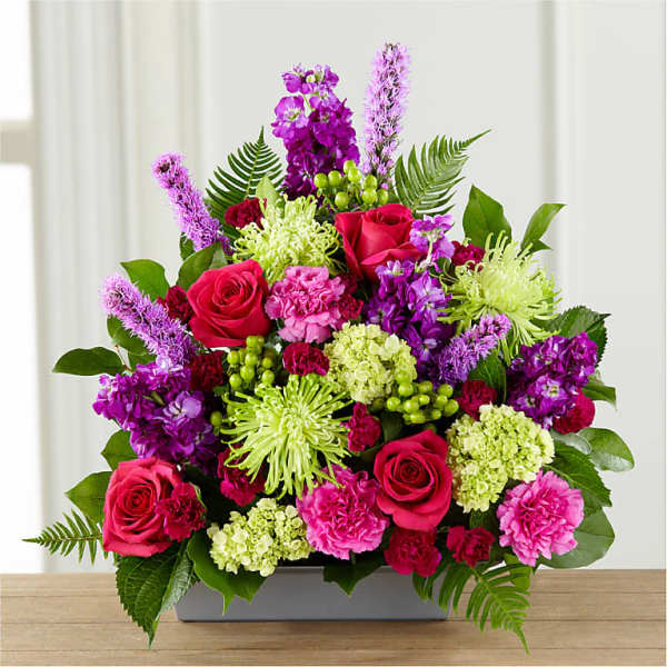 Bright mixed bouquet with roses, carnations, and purple blooms in a low rectangular container