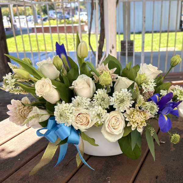 White and cream flower arrangement with blue irises in a white bowl vase