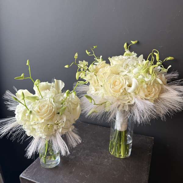 Two ivory bridal bouquets in clear glass vases with feathery accents