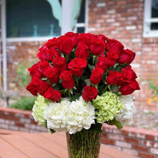Red roses and white hydrangeas arranged in a clear glass vase