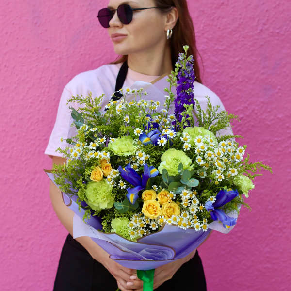 Bouquet of yellow roses, daisies, and purple irises wrapped in lavender paper