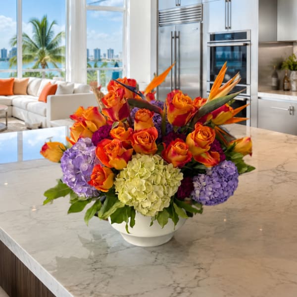 Bright mixed bouquet of orange roses, hydrangeas, and tropical flowers in a white bowl vase