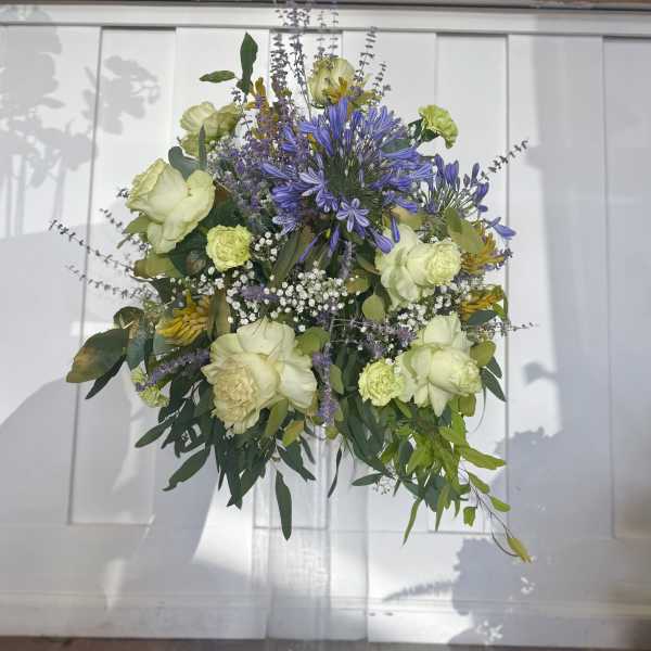 Tall mixed flower arrangement in a clear glass vase with purple and pale green blooms