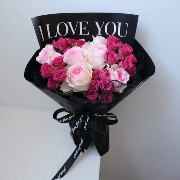 Bouquet of pink and white roses wrapped in black paper with an "I LOVE YOU" sign