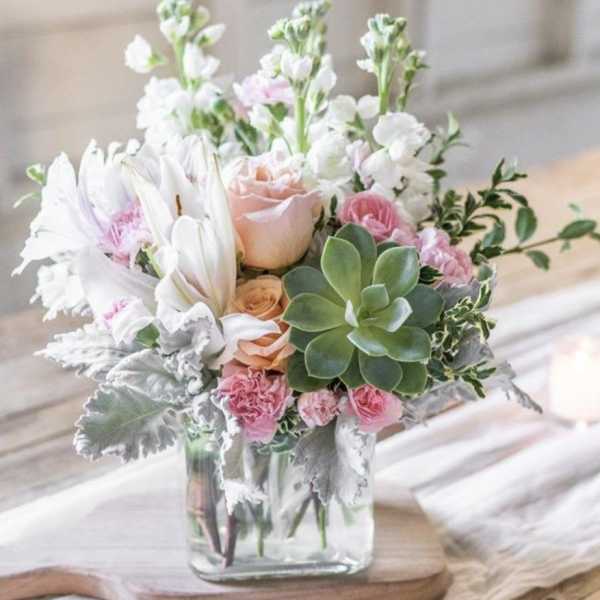Pink and white floral arrangement in a clear glass vase with a succulent