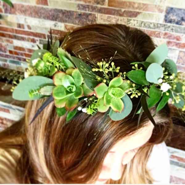 Green floral crown with succulents and small white blooms on a person's head