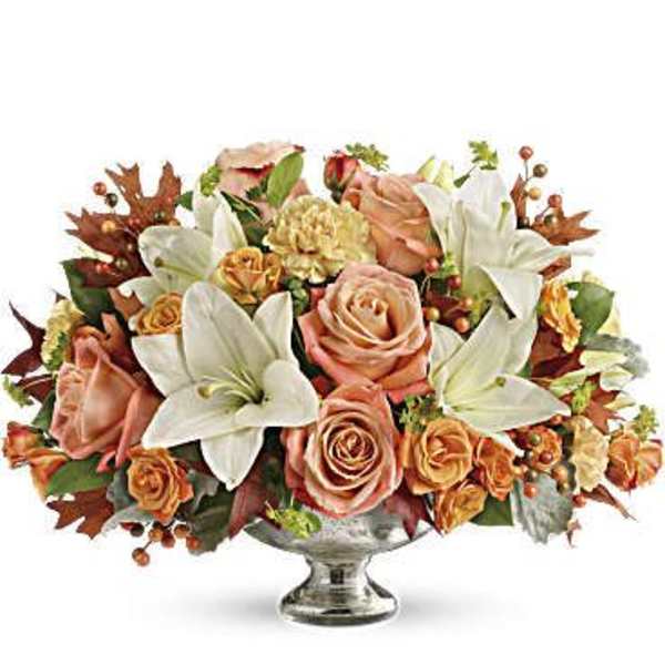 Peach roses and white lilies arranged in a silver pedestal vase