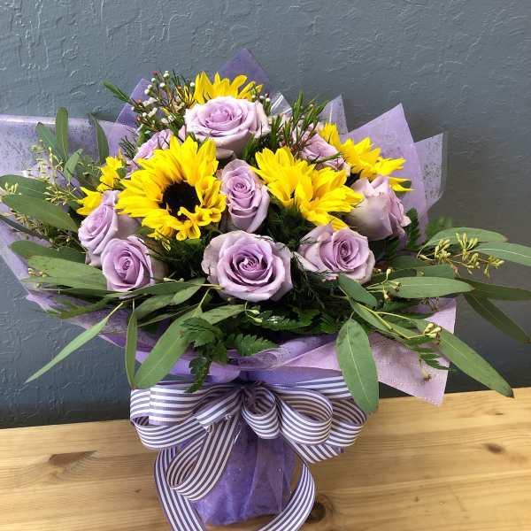 Lavender roses and yellow sunflowers in a wrapped bouquet with a striped ribbon