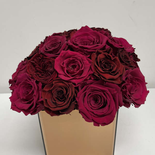 Bouquet of deep pink and burgundy roses in a square gold vase