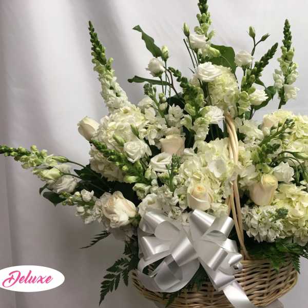 White floral arrangement in a wicker basket with a silver bow