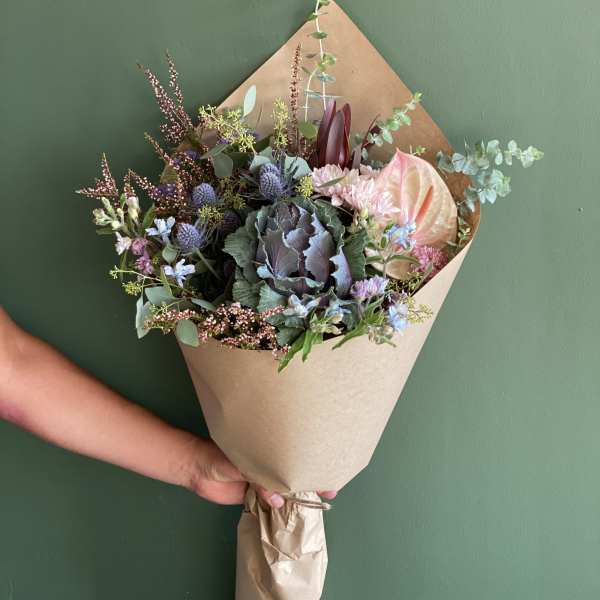 Handheld bouquet with anthurium, thistle, and mixed blooms in kraft paper