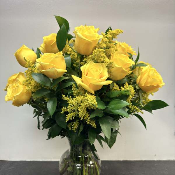 Yellow roses arranged in a clear glass vase with green foliage.