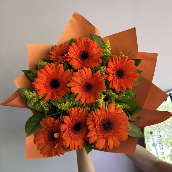 Bouquet of bright orange gerbera daisies with yellow filler wrapped in orange paper