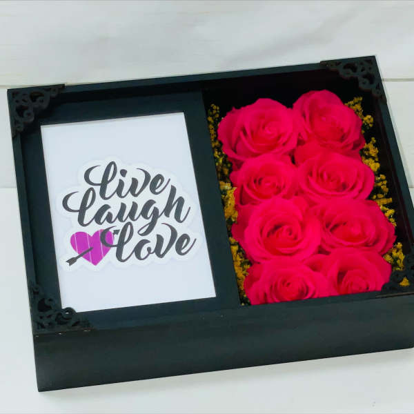 Black gift box with hot pink roses beside a card reading live laugh love