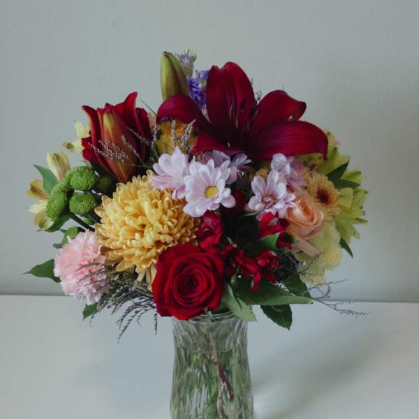 Mixed bouquet of red, pink, yellow, and purple flowers in a clear glass vase