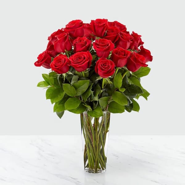 Tall clear glass vase filled with a large bouquet of long-stemmed red roses.