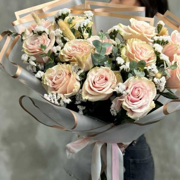 Bouquet of pale pink roses wrapped in translucent paper with ribbon