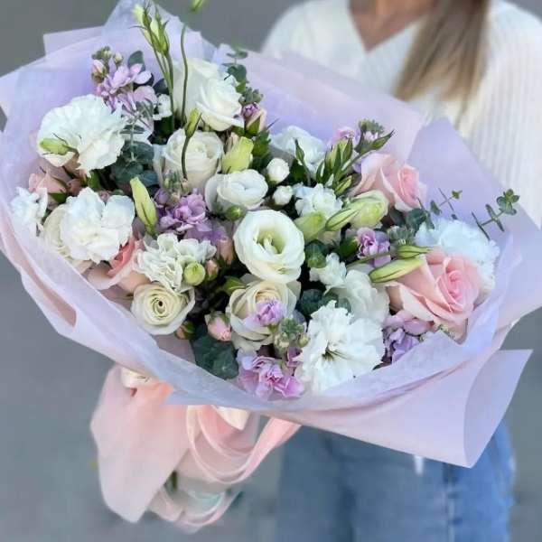 Handheld bouquet of white and blush flowers wrapped in pale lavender paper