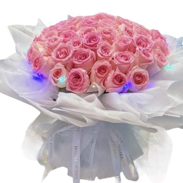 Bouquet of pink roses wrapped in white paper with lights
