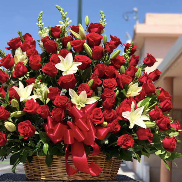 Basket arrangement of red roses and white lilies with a red ribbon