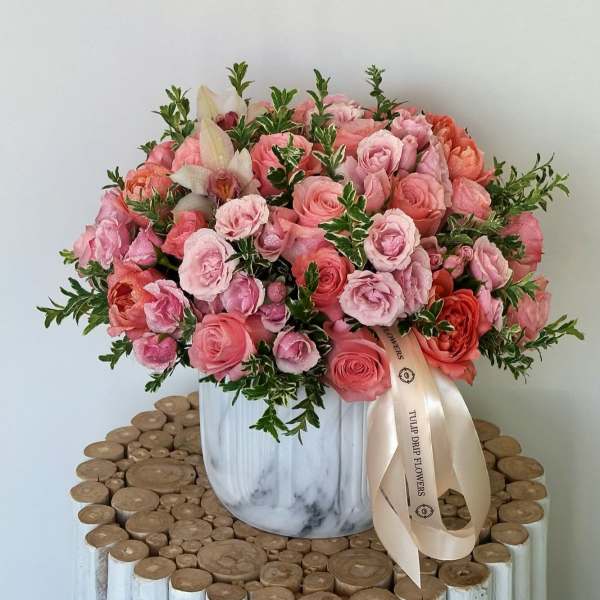 Pink and coral roses arranged in a white vase with a ribbon
