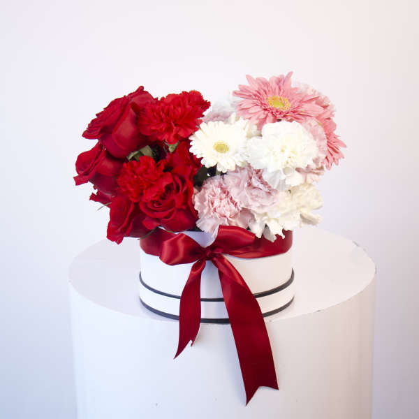 Round box of red, pink, and white flowers tied with a red ribbon