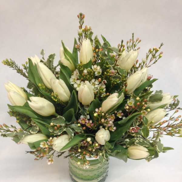 White tulips arranged in a green glass vase with small filler flowers