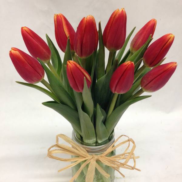 Red tulips in a glass jar tied with a raffia bow