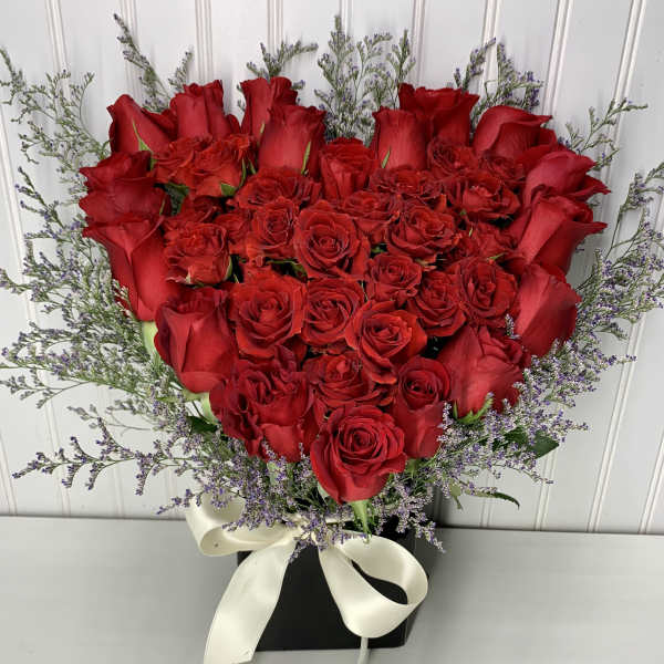 Heart-shaped bouquet of red roses with purple filler and a white ribbon