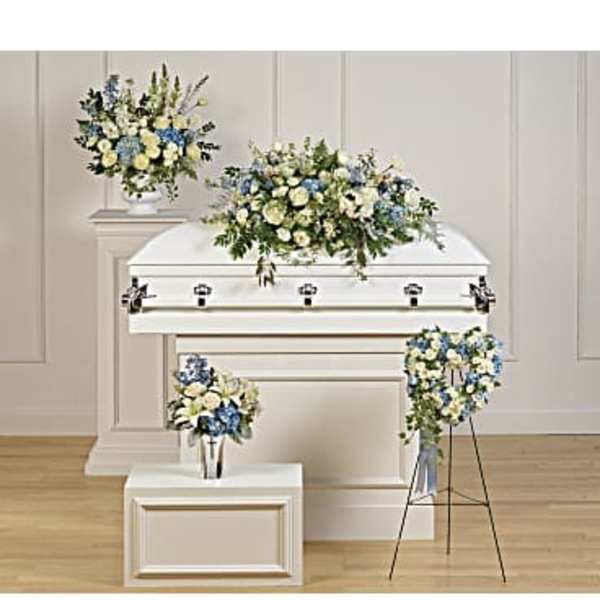 Set of white and blue funeral flower arrangements displayed around a white casket