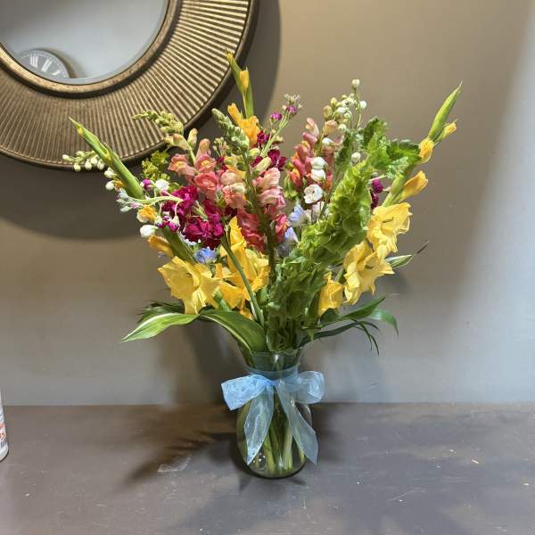 Mixed bouquet of yellow, pink, and white flowers in a glass vase with a blue ribbon