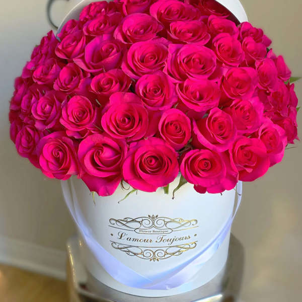 Hot pink roses densely arranged in a white hatbox-style container with gold script text