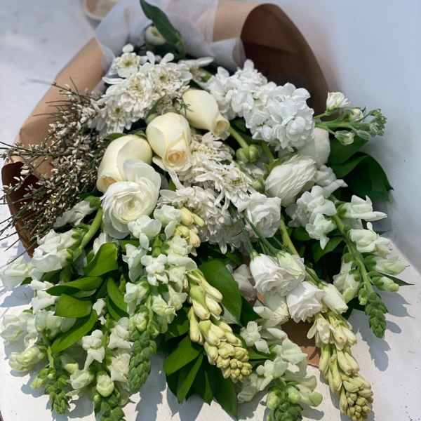 White bouquet with roses and mixed blooms wrapped in brown paper