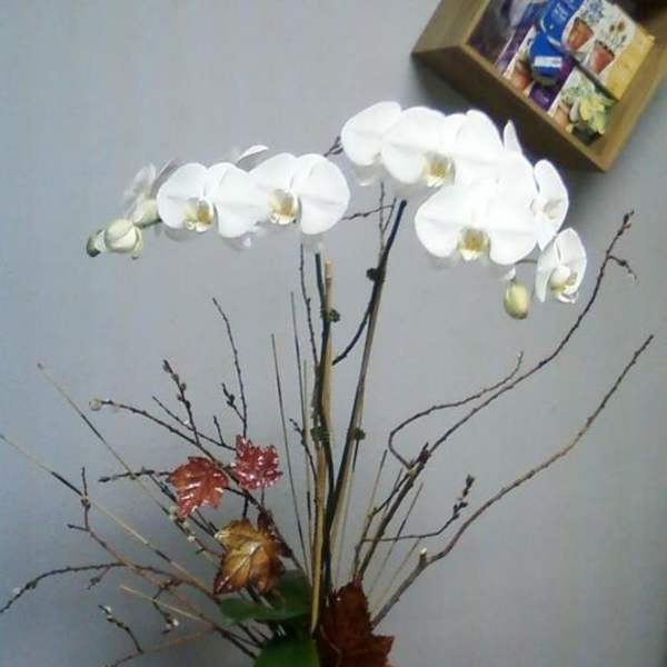 White orchid arrangement in a vase with decorative branches and leaves