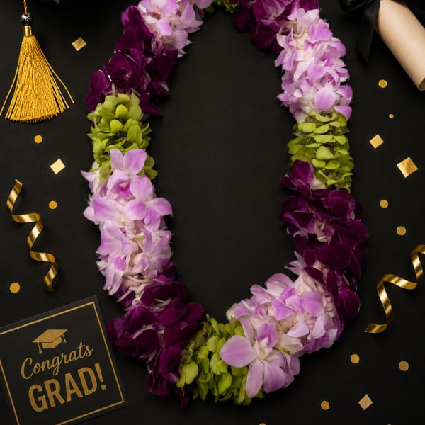 Purple and lavender orchid lei with green accents beside a graduation cap and diploma