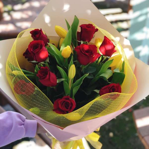 Bouquet of red roses and yellow tulips wrapped in pink paper
