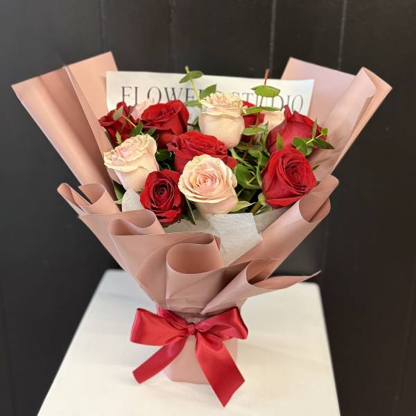 Bouquet of red and blush roses wrapped in pink paper with a red ribbon