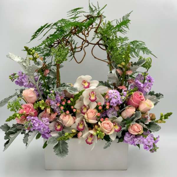 Pink roses and white orchids in a white container with an arching vine frame