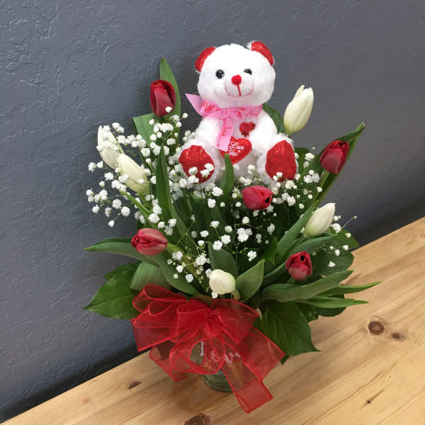 Bouquet of red and white tulips with a teddy bear and red ribbon in a glass vase