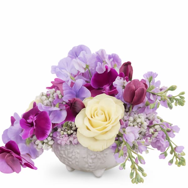 Purple and cream floral arrangement in a white ceramic vase