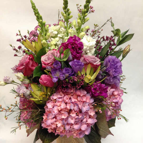 Mixed bouquet of pink, purple, and white flowers in a burlap-wrapped vase