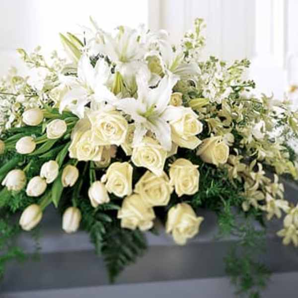 White casket spray of lilies, roses, tulips, and orchids cascading over a gray casket
