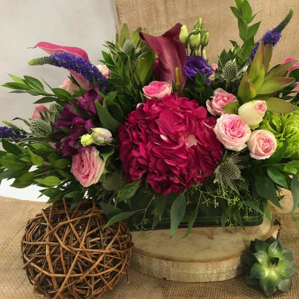 Mixed floral arrangement with pink roses, magenta hydrangea, and purple spikes in a low container