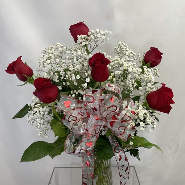 Red roses with white baby's breath in a glass vase, tied with a heart ribbon