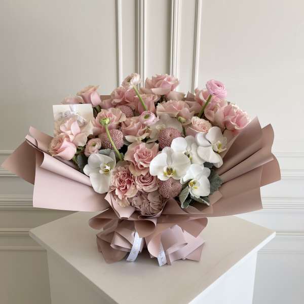 Pink and white bouquet with roses and orchids wrapped in blush paper